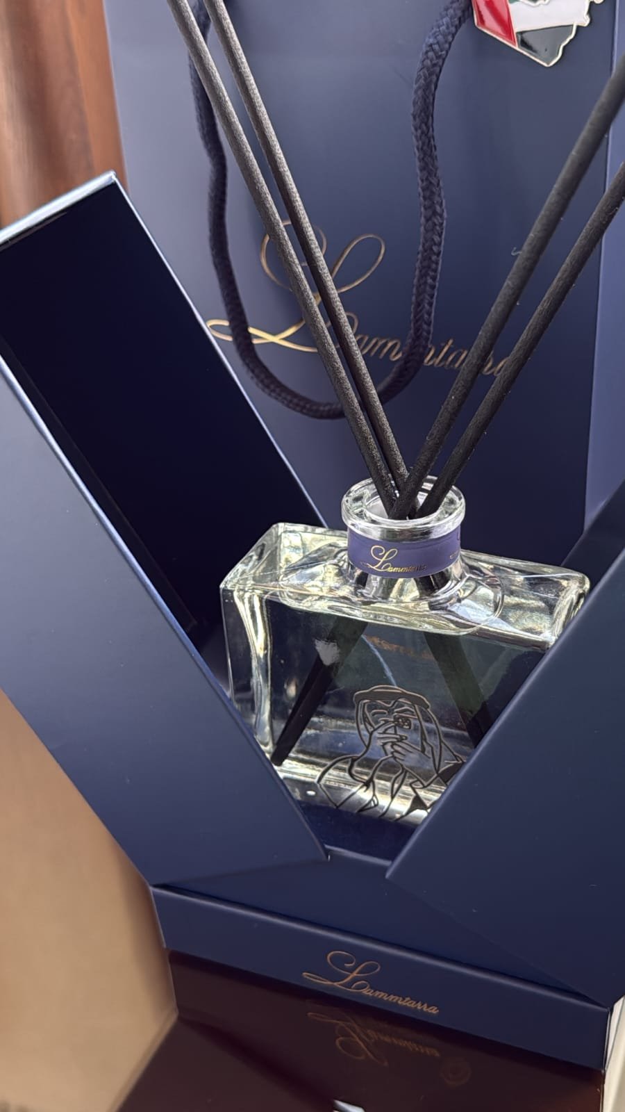 Clear Lammtarra reed diffuser inside its open navy gift box with the gift bag behind