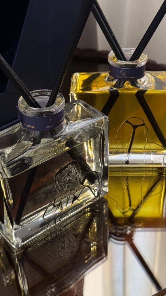 Close-up of the clear and amber Lammtarra diffuser bottles showing the line-art illustrations on the glass